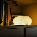 Faltbare Buchlampe aus Holz und Papier mit warmem Licht