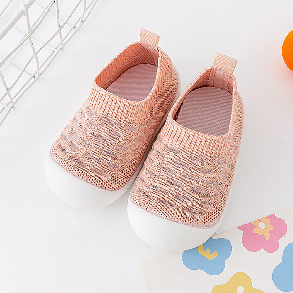 Pink knit baby shoes pair with white soles on colorful play mat