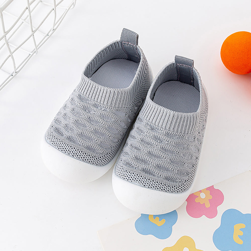 Gray knit baby shoes with slip-resistant white soles on play mat